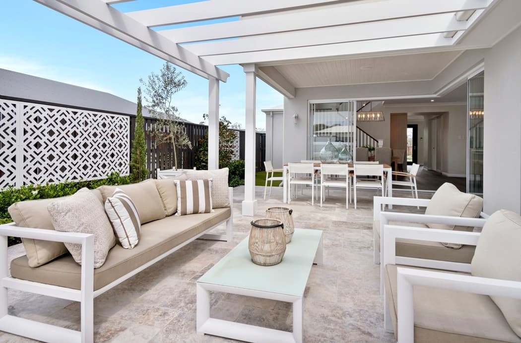 Modern outdoor patio with white pergola, stone tiles, comfortable seating, and a dining area.