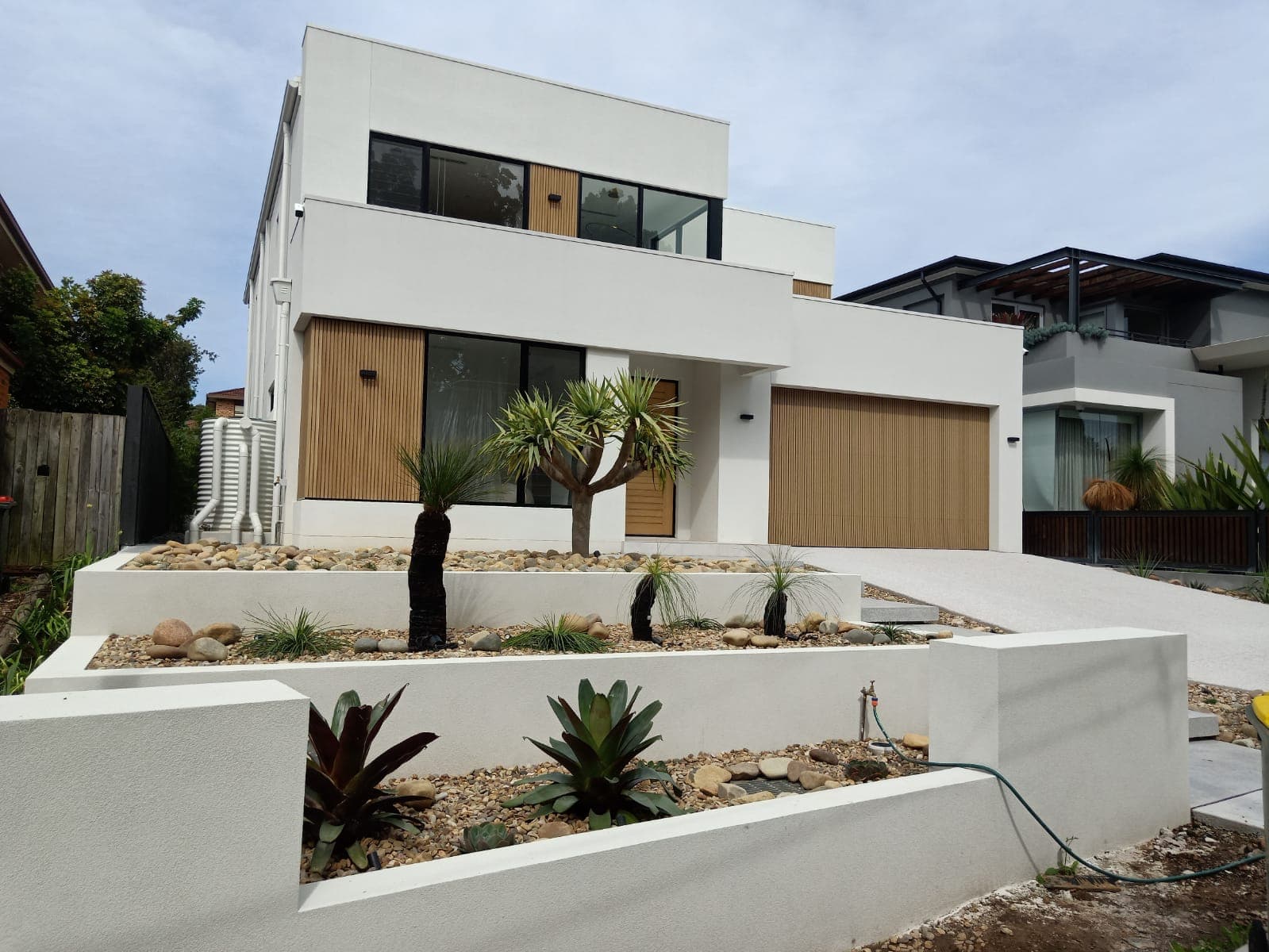 Modern two-story white house with wood accents and tiered rock landscaping with succulents.